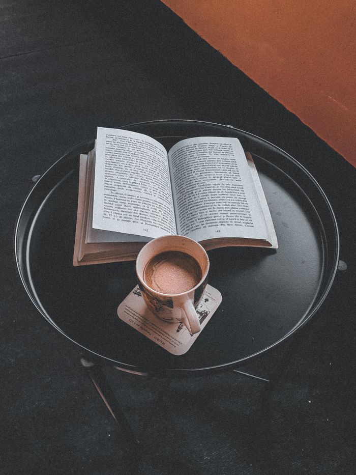 pexels photo 12255407 12255407 An open book and coffee mug on a round black table in a cozy setting, perfect for relaxation.